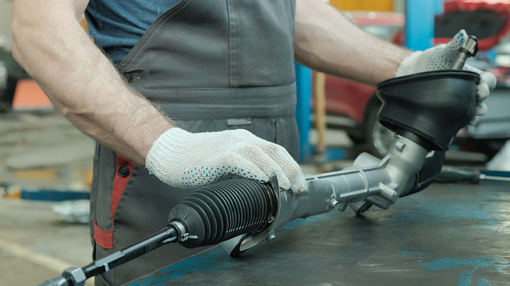 auto mechanic holding a steering rack in hands